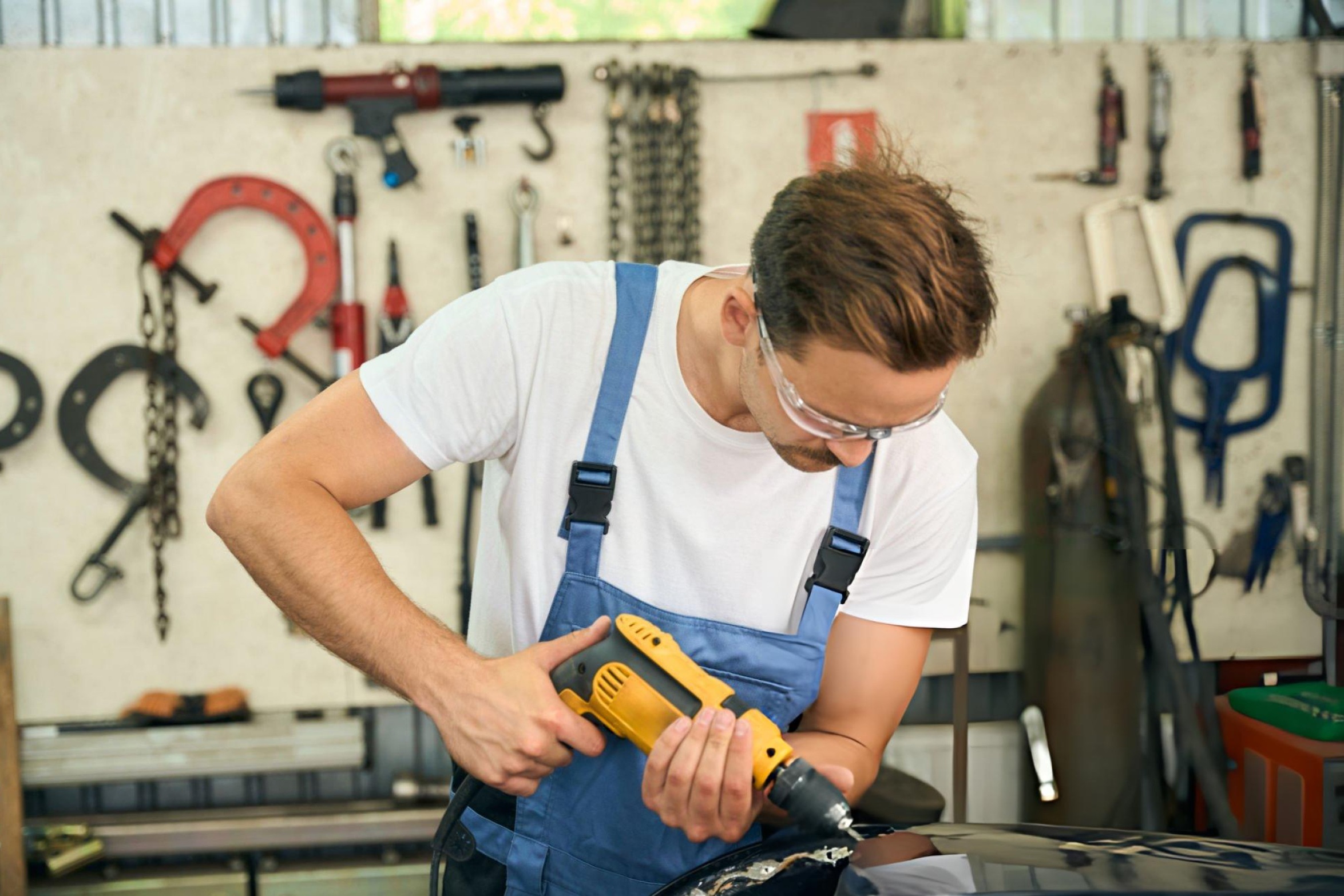 Auto body repair technician using a DA sander on a car panel in a collision repair shop