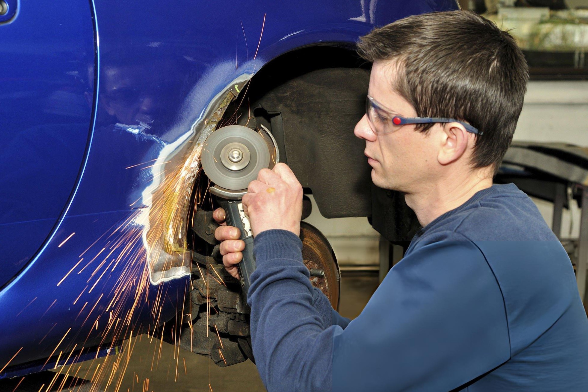 Wide hero image, realistic photo style: a dual-action orbital sander sanding a car body panel in a workshop. Visible sanded area with smooth matte finish. No text, no logos, no watermark